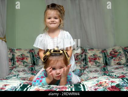 Zwei Mädchen, die ins Bett gehen. Die ältere Schwester hat gewonnen und sitzt auf der anderen. Beide liegen auf dem Bett und im Pyjama. Stockfoto