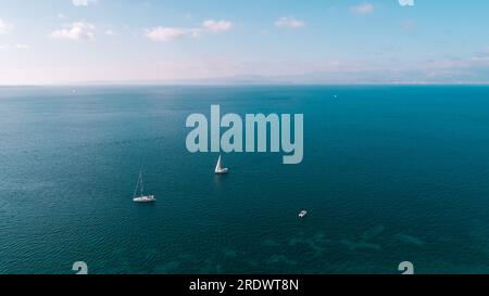 Luftdrohne, ultrabreites Panoramafoto eines wunderschönen Segelboots mit weißen Segelsegeln, das tiefblaues Meer in der Nähe des Zielhafens im Mittelmeer bereist Stockfoto
