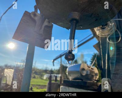 Ein altes rustikales, handgefertigtes Metallwaschbecken mit einem Tropfen sauberem Wasser, das in der Sonne im Dorf baumelt. Stockfoto