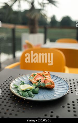 Croissant-Sandwich mit Lachs, pochiertem Ei und Gurke auf dem Teller. Frühstück im Café oder Café. Lifestyles. Stockfoto