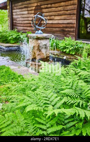 Farnpflanzen wachsen im Sommer vor dem künstlerischen Wasserbrunnen neben der Hütte Stockfoto