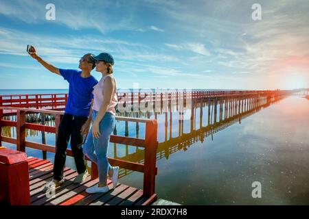 asiatischer Mann und Frau fotografiert mit dem Smartphone an der Red Wood Bridge asiatischer Mann und Frau fotografiert mit dem Smartphone an der Red Wood Bridge Stockfoto