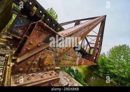 Geneigte Ansicht der Niete auf Metallbalken der alten rostenden Eisenbahnbrücke und des nahegelegenen Flusses Stockfoto