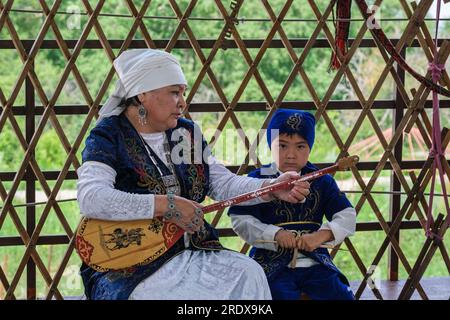 Kasachstan, Hunnen-Ethno-Dorf. Kasacherin in traditionellem Kleid, die Dombra spielt. Stockfoto