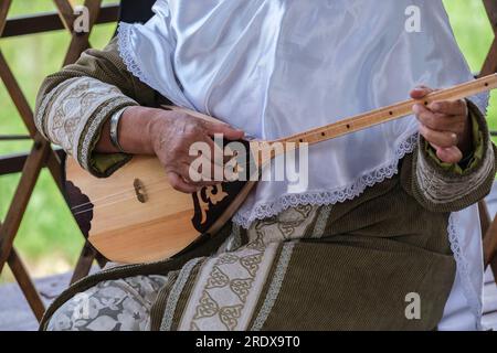 Kasachstan, Hunnen-Ethno-Dorf. Kasacherin in traditionellem Kleid, die Dombra spielt. Stockfoto