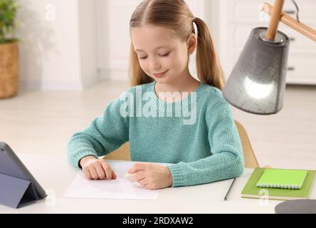 Mädchen, die Radiergummi am weißen Schreibtisch im Zimmer benutzt Stockfoto