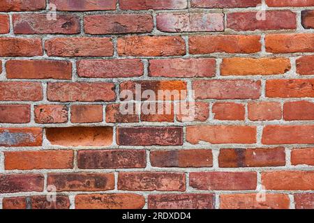 Horizontale Ziegelwand mit einem vertieften Ziegel und schmutziger Oberfläche, wobei die mittlere Reihe kleinere Ziegel sind Stockfoto