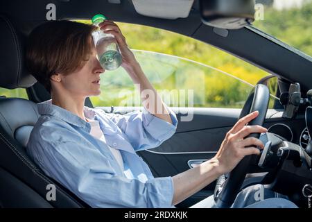 Heißes Wetter für Fahrer. Müde von der Hitze Frau im Auto machen Pause kühle Stirn mit kalter Flasche Stockfoto