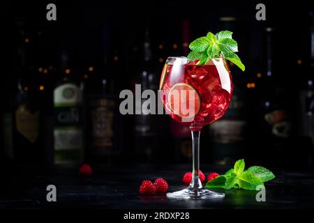 Alkoholische Cocktailgetränke aus königlicher Limonade mit Tequila, trockenem Gin, weißem Rum, Wodka, Likör, Limette, Himbeeren und Eis in Weinglas. Schwarzer Bartresen Ba Stockfoto