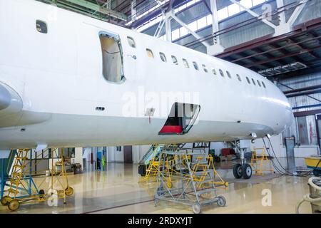 Weißes Passagierflugzeug im Hangar. Luftfahrzeuge werden gewartet. Überprüfung der mechanischen Systeme für den Flugbetrieb Stockfoto