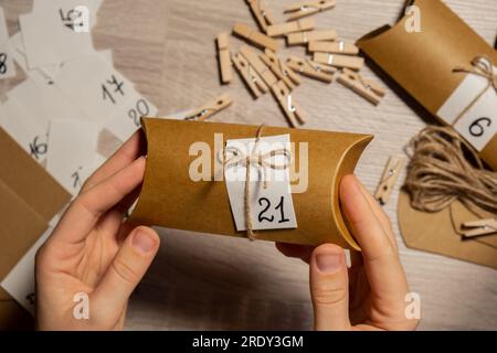 Eine nicht wiedererkennbare junge Frau klebt die Nummer auf die Handwerkstasche, wird mit einer Wäscheklammer befestigt. Weiblich macht Kraftpapier für hausgemachte Adventskalender mit eigenen Händen Schritt für Schritt selbst gemacht. Vorbereitung auf das weihnachtskonzept. Saisonale Aktivitäten für Kinder, Familienurlaub im Winter. Umweltfreundlich Geschenke. Öffnen Sie das Paket jeden Tag Stockfoto