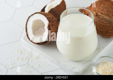 Glas Kokosmilch und Kokosnuss Nahaufnahme auf weißem Hintergrund mit Platz für Text. Vegane Kokosmilch ohne Milchprodukte oder Milchprodukte. Gesund Stockfoto