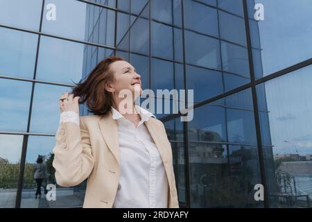 Rücksichtsvolle Geschäftsfrau mit Hand im Haar in der Nähe des Bürogebäudes Stockfoto