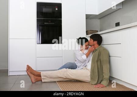 Ein Mann, der eine Frau küsst, die zu Hause in der Küche sitzt Stockfoto