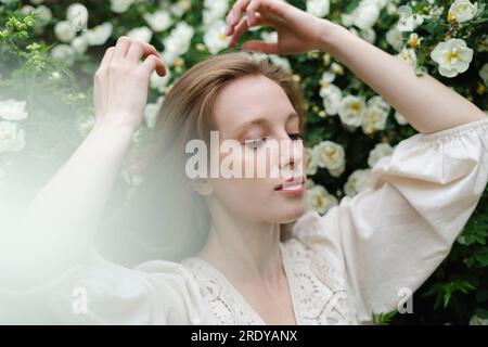 Junge Frau mit Armen, die vom weißen Blumenstrauch gehoben wurden Stockfoto