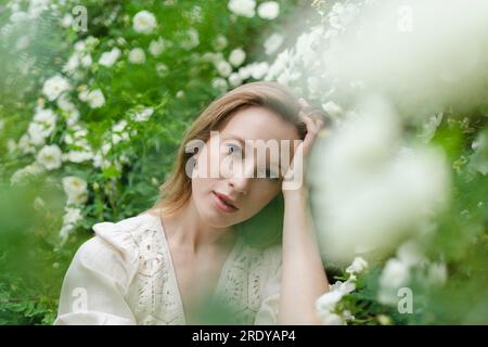 Junge, schöne Frau mit der Hand im Haar im weißen Blumenstrauch Stockfoto
