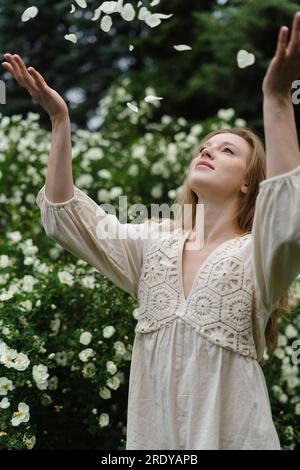 Junge Frau, die Blütenblätter im weißen Blumenstrauch wirft Stockfoto