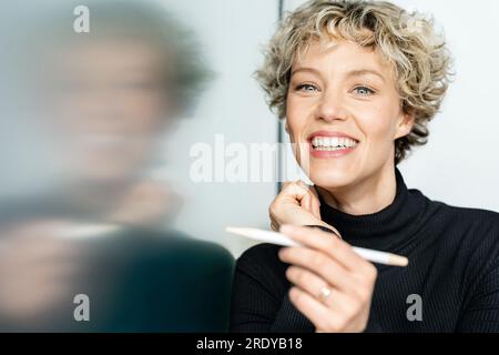 Glückliche Geschäftsfrau mit digitalisiertem Stift, der auf ein interaktives Whiteboard zeigt Stockfoto