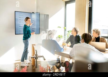 Geschäftsfrau, die auf ein interaktives Whiteboard zeigt und eine Präsentation im Büro hält Stockfoto