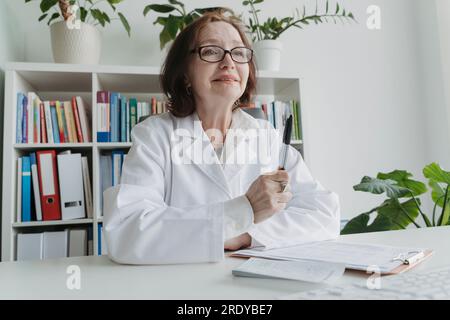 Lächelnder Oberarzt am Tisch in der Praxis Stockfoto