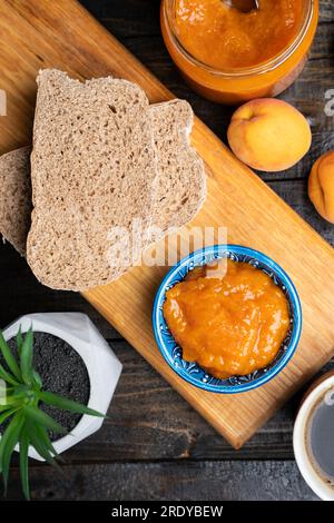 Frische hausgemachte Aprikosenmarmelade in einer blauen Keramikschüssel, Brot und frische Aprikosen auf Holzhintergrund Stockfoto