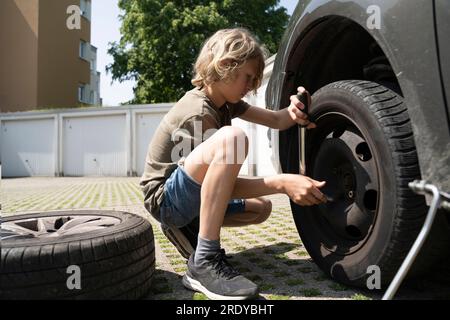 Der Junge wechselt im Hof den Autoreifen Stockfoto