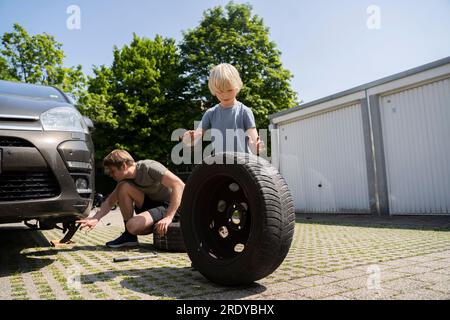 Ein Junge, der Vater beim Reifenwechsel hilft Stockfoto