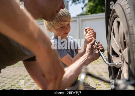 Ein Mann wechselt den Autoreifen mit dem Sohn im Hof Stockfoto