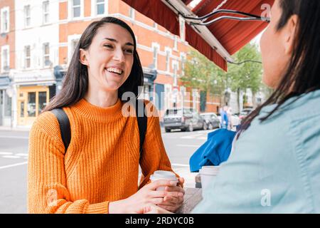 Lächelnde Freunde, die sich unterhalten und Kaffee im Straßencafé trinken Stockfoto