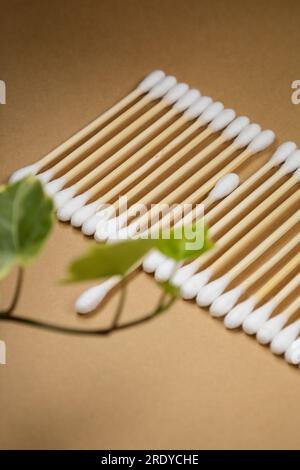 Viele Wattestäbchen aus Holz liegen in einer Reihe auf einem beigen Hintergrund aus Kunsthandwerk. In der Nähe der grünen Blätter der Efeu-Pflanze Stockfoto