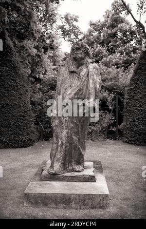 Die Bronzeskulptur von Honoré de Balzac von Auguste Rodin ist von konischen Topien eingerahmt in der Gartenumgebung des Musée Rodin in Paris. Schwarzweißfoto. Stockfoto