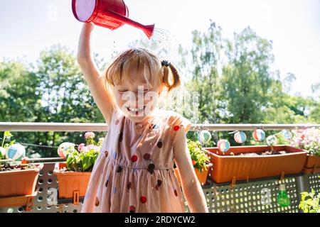 Glückliches Mädchen, das sich auf dem Balkon Wasser gießt Stockfoto