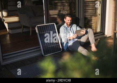 Lächelnder Geschäftsmann, der einen Tablet-PC am Sonnenkollektor auf der Veranda benutzte Stockfoto