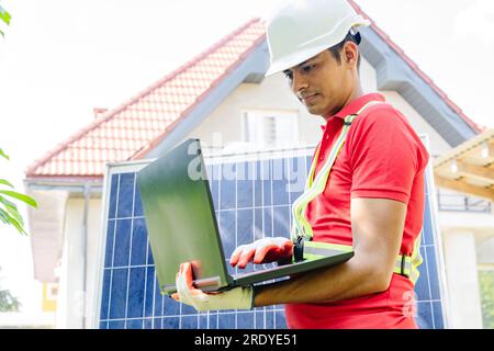 Techniker trägt Schutzhelm mit Laptop am Solarmodul vor dem Haus Stockfoto