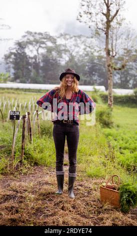 Glücklicher junger Bauer, der auf dem Feld mit den Händen auf der Hüfte steht Stockfoto