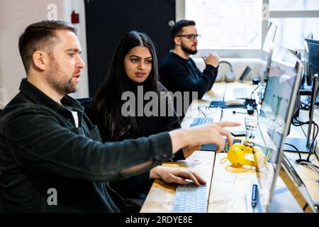 Junge Geschäftsfrau mit Kollegen, die über den Computer diskutieren Stockfoto