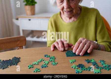 Seniorin löst Puzzle zu Hause auf dem Tisch Stockfoto