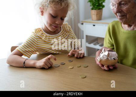 Enkeltochter zählt Münzen von Sparschwein auf dem Tisch Stockfoto