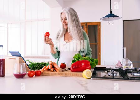 Lächelnde Erwachsene Frau, die zu Hause mit einem Tablet-PC kochen lernt Stockfoto