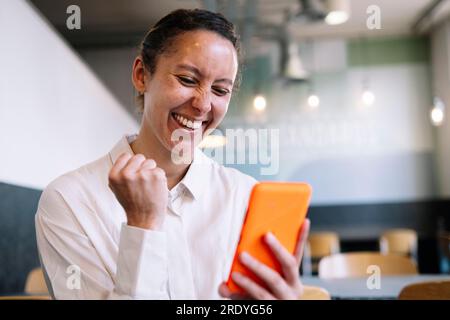 Fröhliche Geschäftsfrau, die im Café Smartphone benutzt Stockfoto