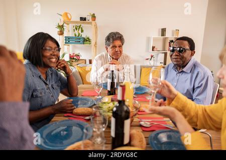 Multikulturelle Seniorenfreunde, die zu Hause am Esstisch zu Abend essen Stockfoto