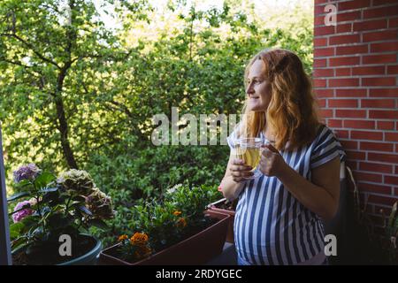 Rücksichtsvolle schwangere Frau hält Kräutertee-Tasse auf dem Balkon Stockfoto