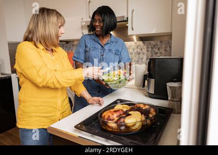 Seniorin, die einer Freundin bei der Zubereitung von Essen zu Hause in der Küche hilft Stockfoto