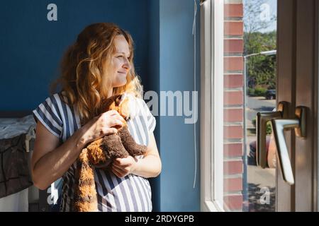 Schwangere Frau hält Stoffspielzeug zu Hause Stockfoto
