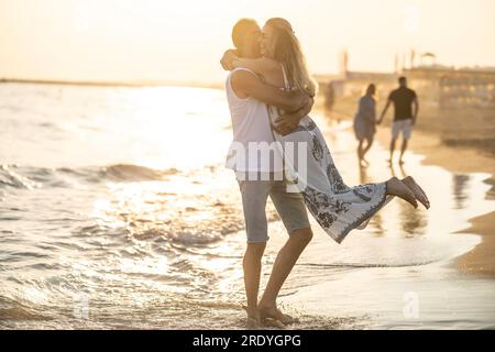 Glückliches Paar mittleren Alters, das sich bei Sonnenuntergang am Strand umarmt. Stockfoto