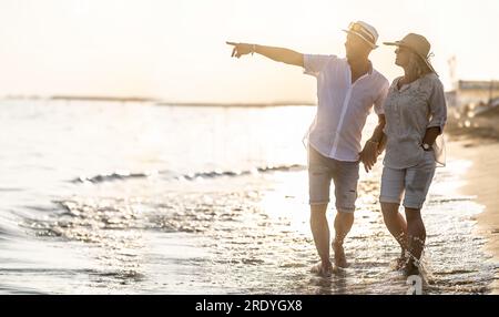 Ein Paar mittleren Alters am Strand bei Sonnenuntergang, der Mann zeigt auf einen Punkt in der Ferne. Stockfoto
