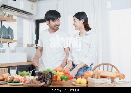 Ein lächelnder Mann umarmte eine Frau, zwei Menschen standen und schauten sich fröhlich an. Ein junges Paar verbringt zu Hause gerne Zeit in einer gemütlichen, modernen Küche. Stockfoto