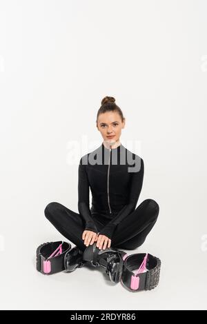 Sprungstiefel, Sportlerin in schwarzem Overall, sitzt mit gekreuzten Beinen, springt kangoo, Stockfoto