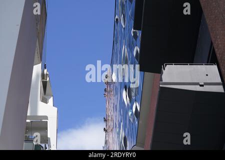 PRODUKTION - 20. Juli 2023, Hamburg: Industrielle Bergsteiger reinigen die Fenster der Konzerthalle Elbphilharmonie im Hafen. Mehrmals im Jahr kommt ein Team furchtloser Kletterer in Hamburg an, um der berühmtesten Konzerthalle der Stadt einen neuen Glanz zu verleihen. Die Glasfassade der Hamburger Elbphilharmonie hat eine Fläche von etwa 16.000 Quadratmetern. Dreimal im Jahr werden die 1100 unterschiedlich geformten Fenster und Glaselemente von professionellen Kletterern gereinigt. Foto: Marcus Brandt/dpa Stockfoto