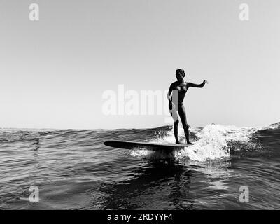 Eine Surferin im Bikini reitet eine kleine Welle, schwarz-weiß Stockfoto